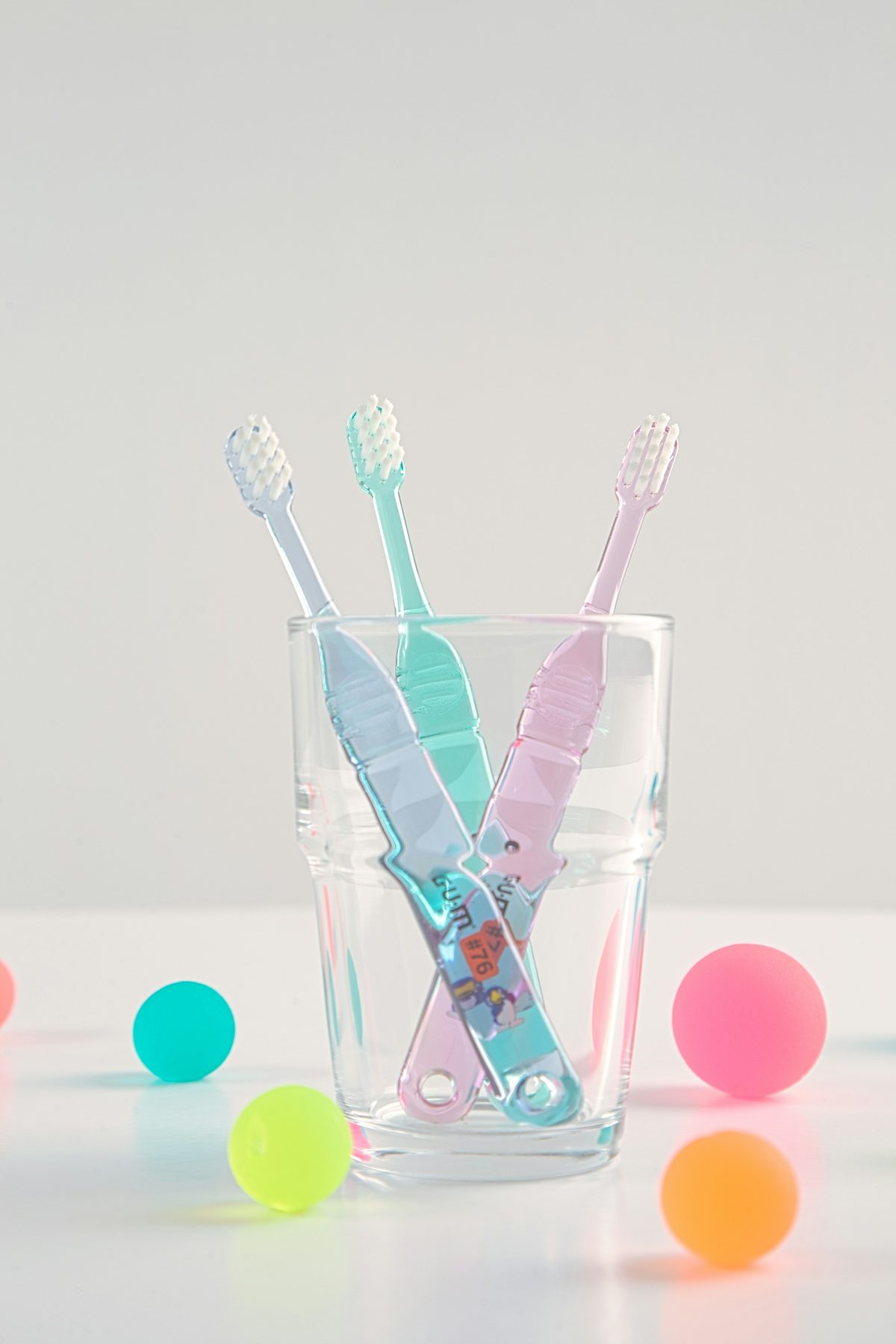 Colorful children's toothbrushes in a glass cup next to playful toy balls